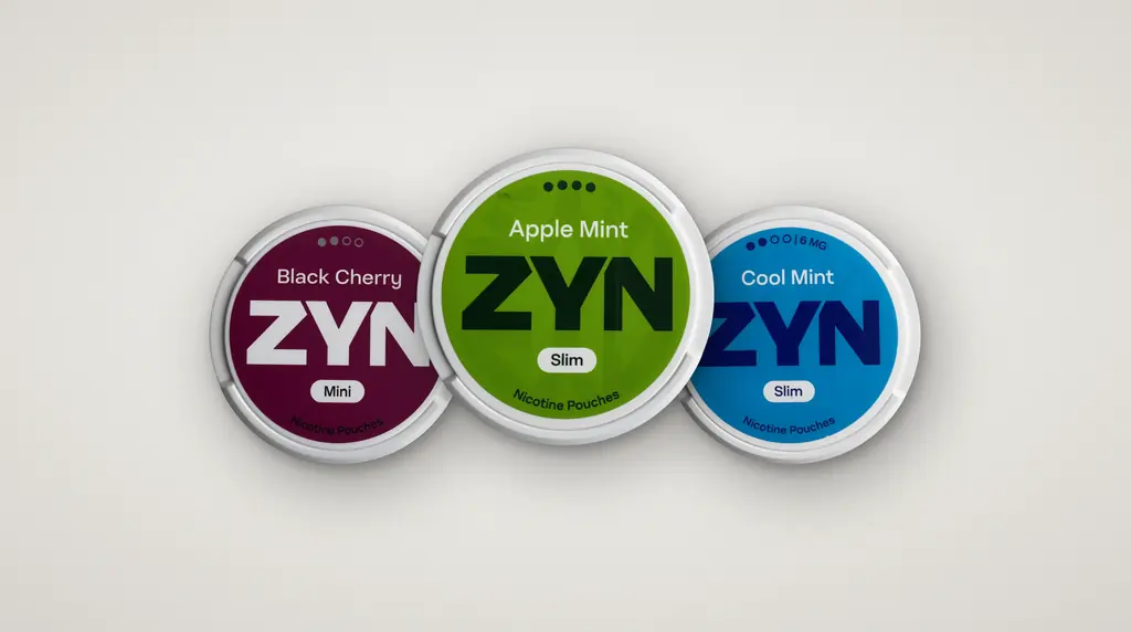 Three ZYN nicotine pouch cans (Black Cherry Mini, Apple Mint Slim and Cool Mint Slim) seen from above on a light grey background
